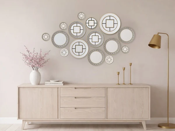 metrochic plates on a wall as art A minimalist living room features a wooden sideboard, decorative circular mirrors on a beige wall, a vase with pink flowers, and a gold floor lamp. Calm, elegant atmosphere.