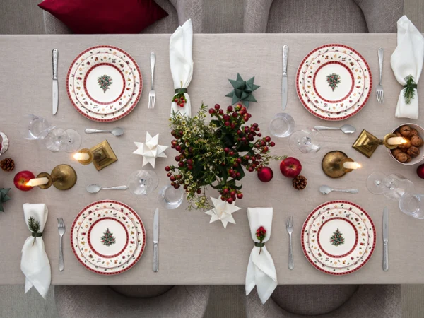Top-down view of a Christmas-decorated dining table for four people with festive plates, candles, and decorative ornaments.