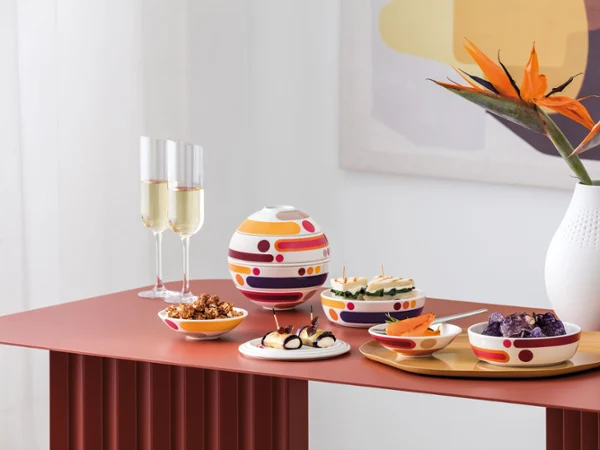 La Boule Miami with Manufacture Blanc Collier Vase in modern arrangement Nowoczesny stół z La Boule Miami, zestawem przekąsek, dwiema kieliszkami szampana i białym wazonem Manufacture Collier z pomarańczowymi kwiatami.