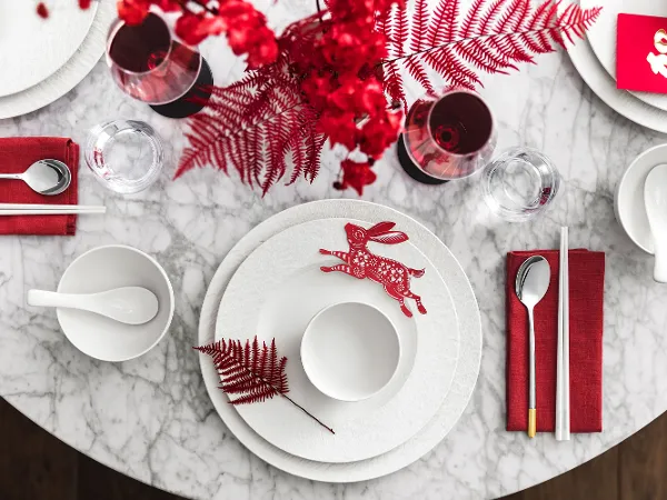 Une présentation de table Manufacture aux notes rouges, composée d’un lapin décoratif et de feuillages rouges sur une surface en marbre.