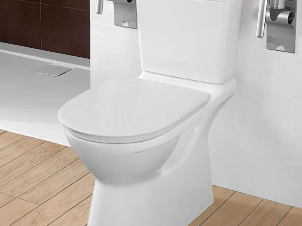 White toilet with metal support handles on both sides, installed on a light wooden floor in a bathroom with white walls.