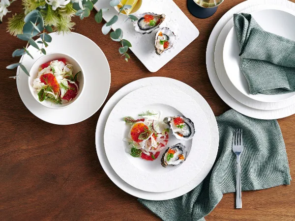 The 8pcs Manufactured Rock dinner set for two, featuring fresh oysters and a side of salad, is complemented by a grey linen napkin on a rustic wooden table, paired with silver cutlery and Manufacture Rock glassware.