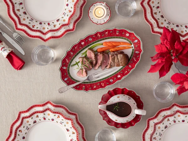 Festive table decoration featuring red and white plates, a roast, carrots, a sauce boat and a red poinsettia as a centrepiece.