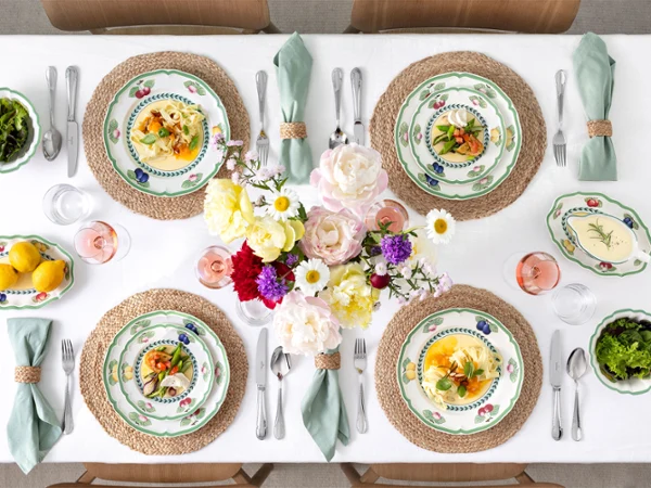 A table set for four with French Garden plates, linen napkins, salads, flowers in the centre and bowls of lemons and greenery