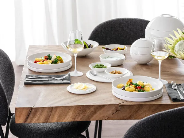 A table set with La Boule with black and grey chairs around it A La Boule table setting with two plates of food, two glasses of white wine, various bowls with side dishes and a flower arrangement with black and grey chairs around the table.