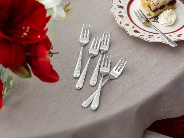Dessert forks for the Christmas season Five dessert forks on a beige tablecloth next to a plate with cake and whipped cream and a vase with red flowers.