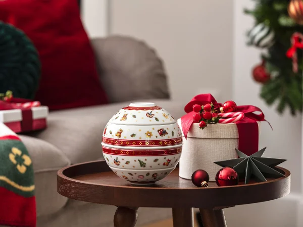 Un tavolino rotondo con un set decorativo di ciotole sferiche, una confezione regalo e palline in un ambiente festivo del soggiorno.