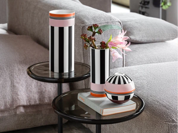 Two black and white striped vases stand on glass tables Two black and white striped vases and a round vessel stand on glass tables next to a grey sofa, flowers in a vase