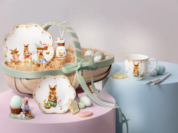 Annual Easter Edition 2026 tableware with bunny designs, eggs, a mug, and cookies arranged on pastel-colored platforms.