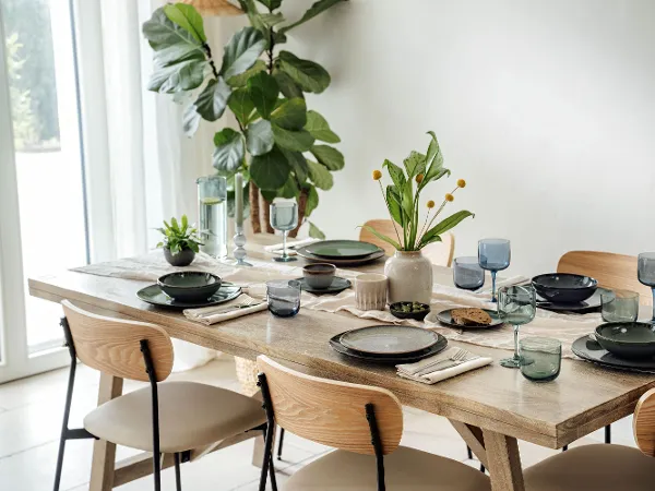 Esstisch für sechs mit Lave-Tellern von Villeroy & Boch“ Gedeckter Esstisch für sechs Personen mit Tellern der Kollektion Lave von Villeroy & Boch, Gläsern und Pflanzen als Mittelstück in hellem Raum.“