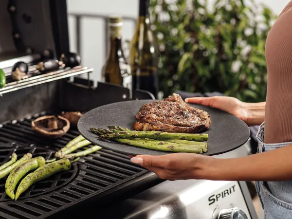 Stilvolles BBQ-Set mit schwarzem Manufacture Teller und Frau am Grill Ein stilvoll gedeckter Tisch mit schwarzem Manufacture Teller als Teil eines BBQ-Sets, während eine Frau am Grill steht – moderne Eleganz für Grillabende.
