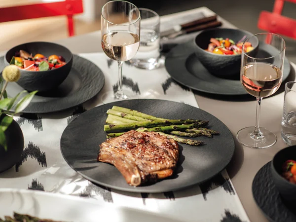 Elegantes Grillessen mit Steak und Spargel auf einem Manufacture Teller, dazu Wein und Salat.