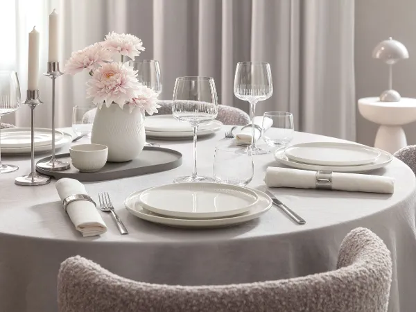 Round dining table with white Afina plates Round dining table with white Afina plates, Afina glasses, cutlery, napkins and a vase with pink flowers.