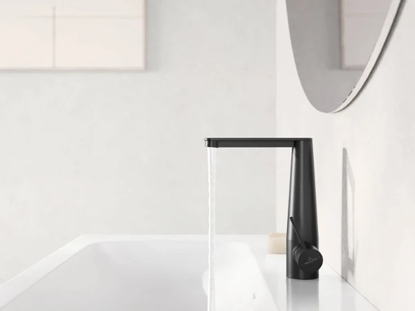 Une robinetterie de lavabo noire Conum d’où s’écoule de l’eau Un robinet noir moderne d’où de l’eau s’écoule dans un lavabo blanc. Un miroir partiellement visible sur le côté droit reflète la scène.