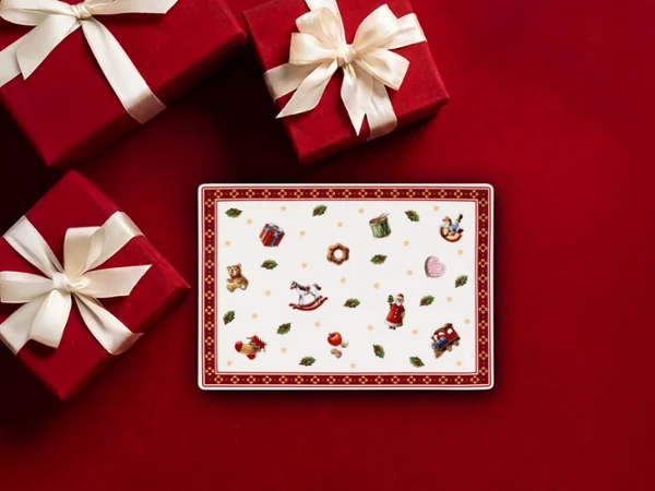 Tres cajas de regalo rojas con lazos blancos y un plato rectangular festivo sobre un fondo rojo.