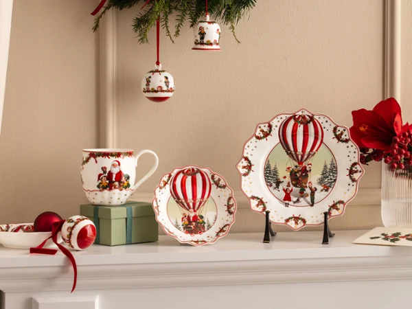 Annual Chistmas edition 2026 collection Festive ceramic plates, cups, and bowls with motifs of red hot air balloons from Villeroy & Boch are presented together with red flowers and Christmas decorations.