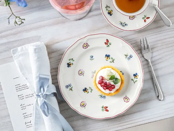 Petite Fleur plate with a cake and a teacup Petite Fleur plate with a cake, a teacup, a drink with a flower and a napkin on a wooden table.