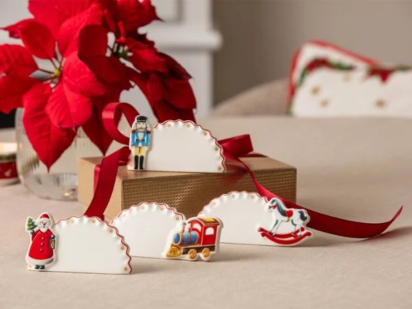 Festive place cards decorated with Christmas figures A table with festive place cards decorated with Christmas figures, a red ribbon and poinsettias in the background.