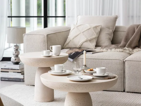 White Afina coffee crockery in a modern, bright living room A cosy, modern living room with a beige sofa, round coffee tables with a modern coffee set with cups and plates from the Villeroy & Boch Afina collection.