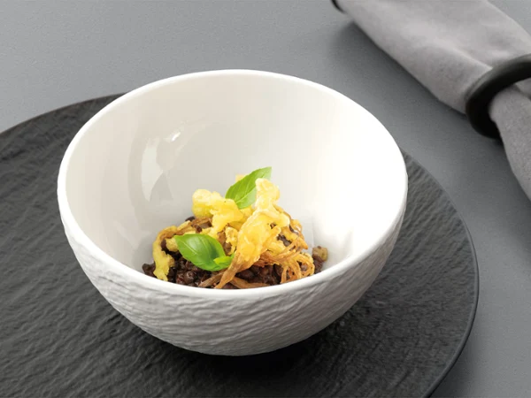 Manufacture bowl on top of a plate Manufacture white bowl on a black plate, with food in the bowl.