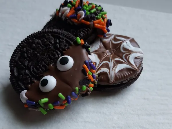 Three Halloween cookies with candy eyes, colorful sprinkles, and swirled frosting on a white, textured surface.