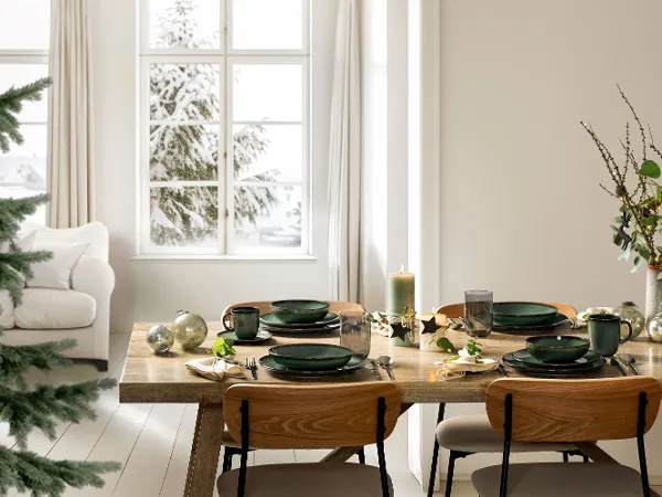 Modern Christmas Table with Lave Vert – Festive Winter Mood A bright and festive winter table setting featuring four place settings from Villeroy & Boch’s Lave Vert collection, including dinner plates, bowls, and handled mugs. The modern arrangement is complemented by a decorated Christmas tree and subtle seasonal decor, creating a serene holiday atmosphere with natural tones and handcrafted charm.