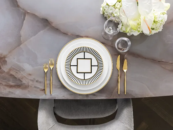 Stylish plates and dishes with elegant MetroChic dinnerware and golden MetroChic flatware Stylish dinner service with elegant MetroChic dinnerware, gold flatware, and a floral centerpiece on a marble table.