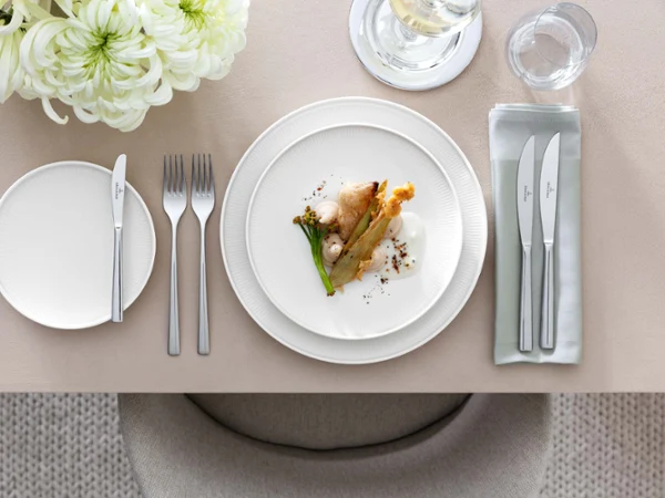 White Afina dinner plate with Piemont cutlery Elegant table decoration with a white Afina gourmet plate, Piemont cutlery and floral decoration.