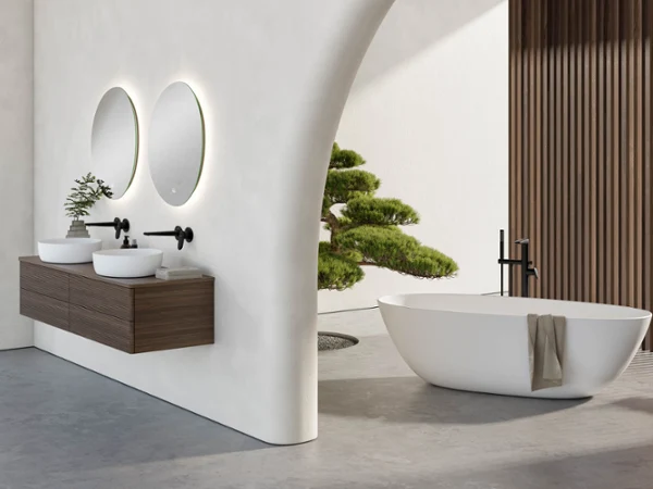 Łazienka wellness Antao z umywalką podwójną i wanną wolnostojącą Nowoczesna łazienka z dwoma okrągłymi lustrami, wiszącą drewnianą szafką podumywalkową, umywalką podwójną, czarnymi bateriami, wanną wolnostojącą Antao z ręcznikiem i minimalistyczną rośliną pokojową obok ściany wyłożonej drewnianymi listwami.