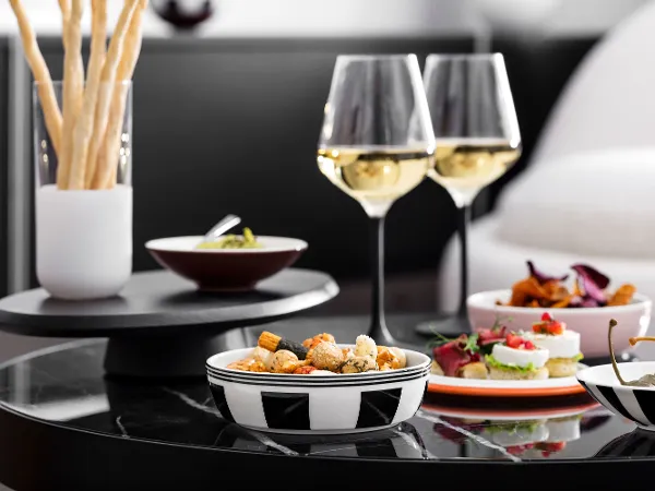 La petite Boule filled with nibbles and Manufacture white wine glasses A black table with La petite Boule individual bowls filled with nibbles and Manufacture white wine glasses.