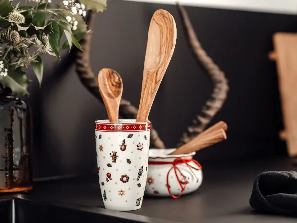 Dwie drewniane łyżki w kubku Toy's Delight To Go na czarnym blacie kuchennym Dwie drewniane łyżki w kubku Toy's Delight To Go i drewniana chochla w białej misce z czerwoną obwódką, ułożone na czarnym blacie kuchennym, z elementami dekoracyjnymi w tle.