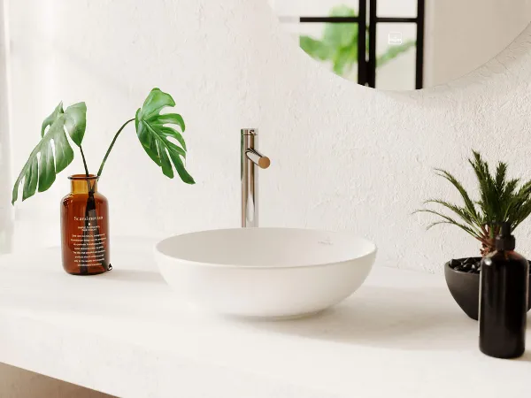 Weißes Loop & Friends Waschbecken auf in einem modernen hellen Badezimmer Moderne Badezimmerwaschtischplatte mit weißem Loop & Friends Aufsatzwaschbecken und Armatur neben dekorativen Pflanzen in orangefarbenen und schwarzen Vasen
