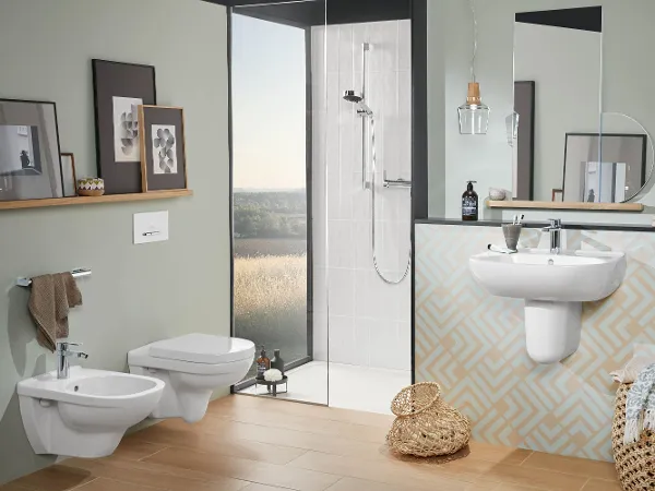 Modernes Bad mit WC, Bidet, Waschbecken und Dusche aus der Kollektion O.novo Das moderne Bad mit beigefarbenen Fliesen und pastellfarbenen Wänden ist mit einem O.novo-Wand-WC, einem Bidet, einem Waschbecken mit Spiegel und einer bodengleichen Dusche ausgestattet. Die Regale sind mit gerahmten Kunstwerken und Toilettenartikeln bestückt. Auf dem Boden stehen Körbe.