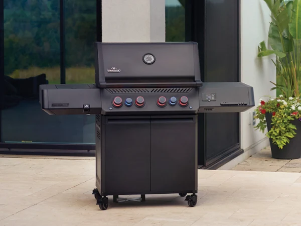 Eine moderne Terrasse mit Gasgrill, Esstisch für draußen und Gartenstühlen neben einem zeitgenössischen Haus mit Blick auf eine malerische Landschaft.