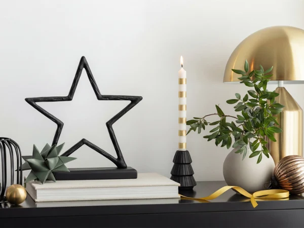 On a tabletop decorated with ornaments On a tabletop decorated with ornaments, there is a black star-shaped sculpture, a striped candle, a small plant and a golden lamp.