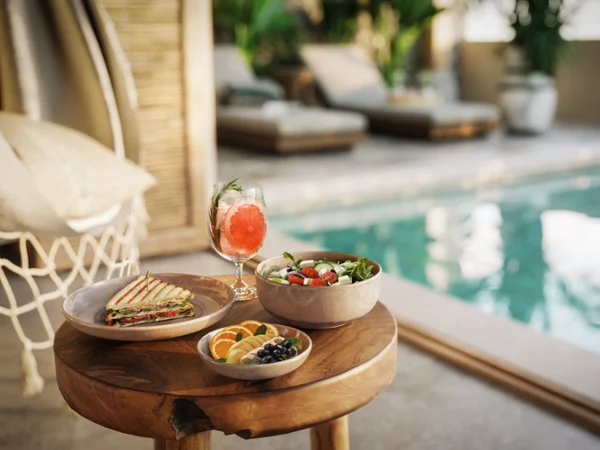 Poolside Brunch with Salad, Sandwich, and Cocktail Poolside summer lunch with salad, grilled sandwich, fresh fruit, and a citrus cocktail served on natural stoneware tableware in a luxurious outdoor setting.