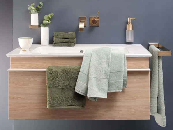 Handtücher One in Grün über Schrankwaschtisch Modernes Badezimmer mit Schrankwaschtisch, Unterschrank aus Holz und grünen Handtüchern. Goldene Armaturen und Pflanzendekor an einer grauen Wand.