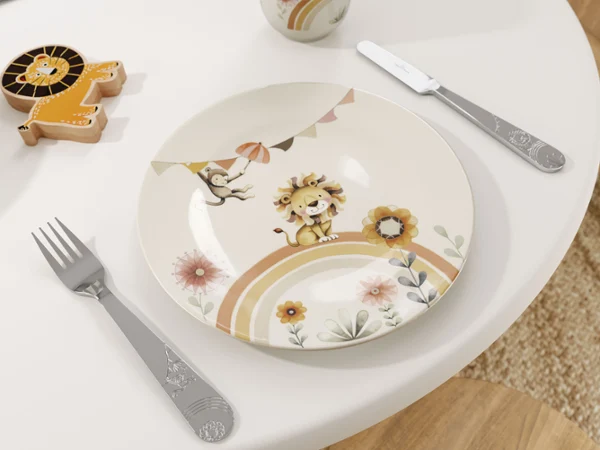 Boho Kids | Roar like a Lion by Villeroy & Boch - Plate and Cutlery The Boho Kids | Roar like a Lion children's plate by Villeroy & Boch features a lion design on a table with a fork and knife, complemented by a lion-shaped toy figure in the background.