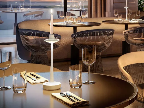 Eine Aarhus Leuchte in Form eines Kerzenständers Elegantes Restaurant-Interieur mit gedeckten Tischen, Gläsern, Servietten und einem modernen Kerzenständer mit Blick auf große Fenster.