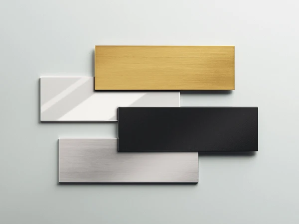 Quattro piastre metalliche rettangolari in tonalità oro, nera e due argento, disposte sovrapposte su uno sfondo chiaro.