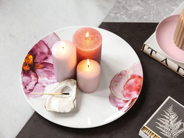 Rose Garden plate with floral decor and lit candles on top Decorative Rose Garden plate with lit candles next to a shell and a book with a gold leaf pattern.