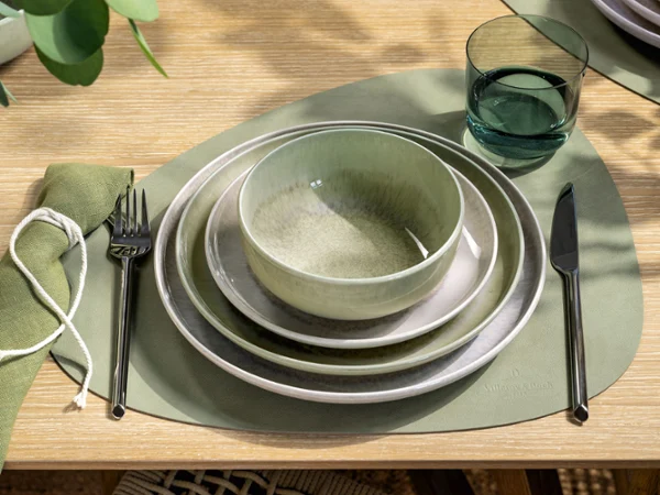 A modern table with green and beige crockery A table set with green and beige crockery, a bowl, a glass, cutlery and a green placemat.