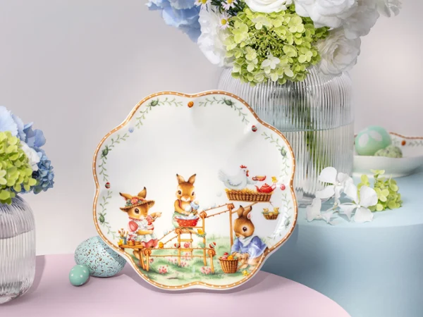 Decorative Annual Easter Edition plate with animal illustrations, displayed among vases of flowers and pastel-colored eggs on a table.