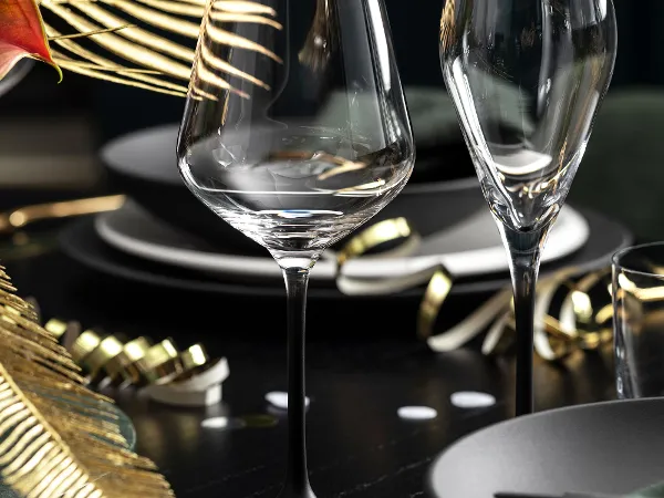 Une table de salle à manger élégamment dressée avec deux verres à vin Villeroy & Boch Manufacture, des assiettes noires et des éléments décoratifs dorés, dont une feuille de fougère.