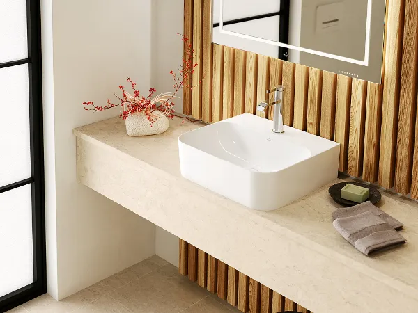 Finion Aufsatzwaschbecken mit Chromarmatur in hellem Naturtönebad Minimalistisches Badezimmer mit einem rechteckigen Aufsatzwaschbecken, einer Armatur, einem zusammengerollten Handtuch, einer Seifenschale mit Seife und einer kleinen Vase mit roten Zweigen auf einer hellen Arbeitsplatte.