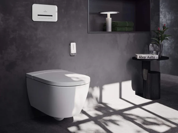 Szafka podumywalkowa cała w czerni Czarna szafka łazienkowa Subway 3.0 z białą umywalką podwójną i czarnymi bateriami, montowane na ścianie lustro My View Now firmy Villeroy & Boch oraz przedmioty dekoracyjne, takie jak dozowniki do mydła i ręczniki ułożone w stos.