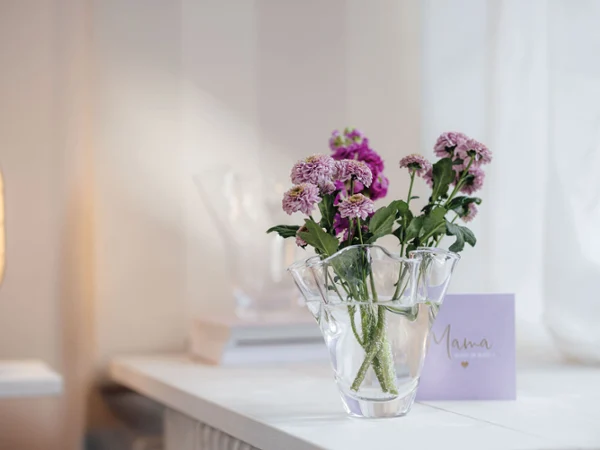 Un jarrón Blossom con flores moradas sobre una mesa Un jarrón con flores moradas sobre una mesa, junto a él una tarjeta con la inscripción "Mamá".