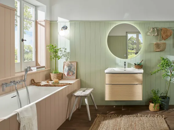 Badezimmer mit einer Subway 3.0 Badewanne von Villeroy & Boch Badezimmer mit einer Subway 3.0 Badewanne von Villeroy & Boch, rundem Spiegel und Holzwaschtisch. Pflanzen und Korbdekor verleihen eine natürliche Note. Holzvertäfelungen in Pastellfarben unterstreichen die rustikale Ästhetik. Licht strömt durch das Fenster herein.