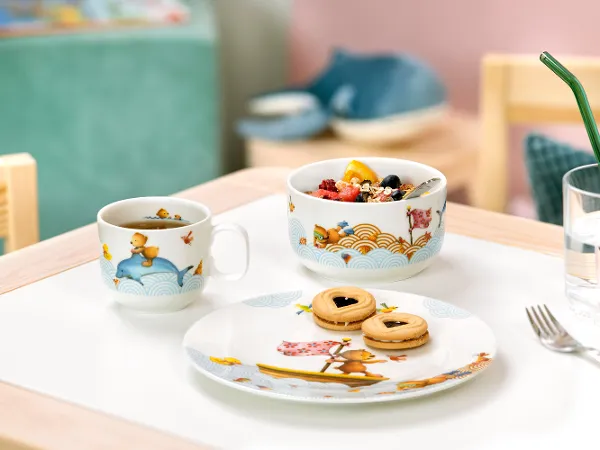 Zestaw śniadaniowy Kiddy Bears ze śniadaniem na stole Zestaw śniadaniowy Kiddy Bears z dekorowanym kubkiem, miską na owoce i talerzem z ciastkami na stole.