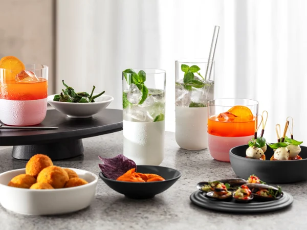 Contemporary Entertaining with Cocktails and Small Bites Assorted appetizers and refreshing cocktails served in modern frosted glassware and minimalist bowls on a stone countertop. The spread features citrus cocktails, sparkling mint drinks, savory bites, and colorful snacks, creating a stylish setting for contemporary entertaining.